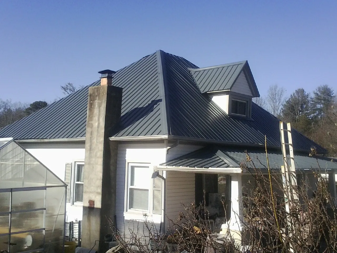Dark blue standing seam metal roof on a white farmhouse with dormer — Slate & Tile Roof Repair by Roofing Brothers in Adamsville