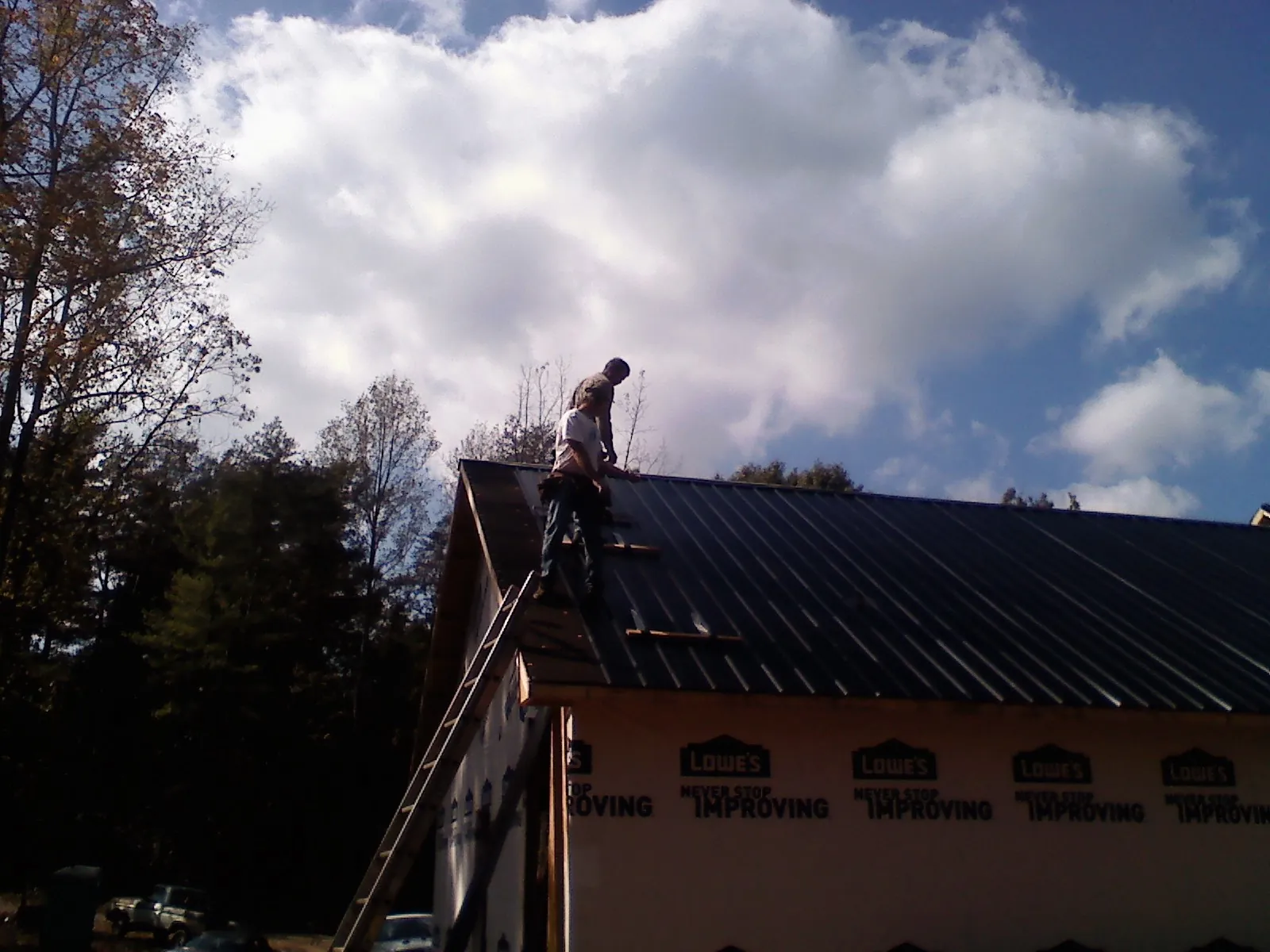 Roofer fastening dark metal panels high against a cloudy sky, from a Roof Inspection job in Adamsville